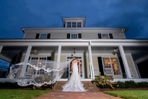 Wedding Vendor Ben Belt Photography- Bride's veil blowing in the wind while standing in front of an old southern house - Forever Bridal Wedding Shows