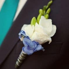 Boutonniere of white and blue flowers on suit