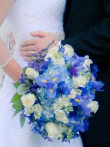 Bride and groom holding each other and bride is holding an assortment of blue and white flower bouquet