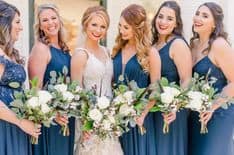 Bridesmaid in blue dresses with the bride in the middle with her white gown - everyone is holding their flower bouquet 