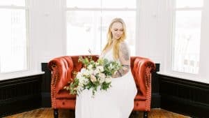 The yellow house at west meadows bride sitting on red couch indoors holding bouquet