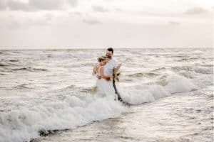 Sinderellas Rockefellas Bridal Boutique Beach Couple Photoshoot couple standing in water as waves crash the beach