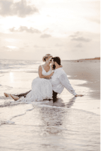 Sinderellas Rockefellas Bridal Boutique Beach Couple Photoshoot Bride sitting on Grooms lap as the waves crash on the beach