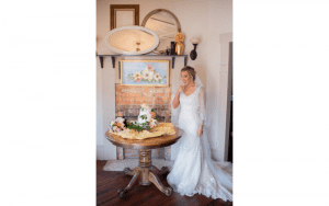 Sinderellas Rockefellas Bridal Boutique image of bride standing next to her wedding cake indoors in gown and veil