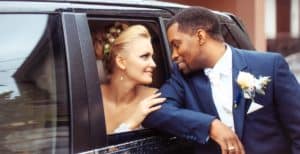 A bride sits inside a Triangle Corporate Coach vehicle with her groom outside of the vehicle.