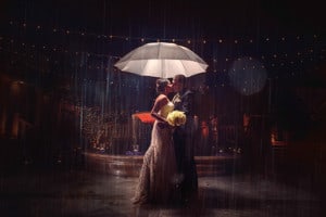 Newlyweds embrace in the rain under an umbrella