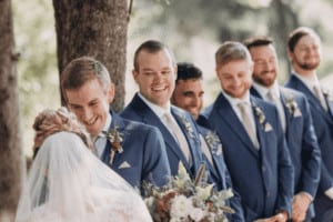Groomsmen dressed in matching suits stand behind a bride and groom.